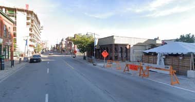 Wide daytime street view of a city block with low-rise commercial buildings and roadworks barriers along the kerb